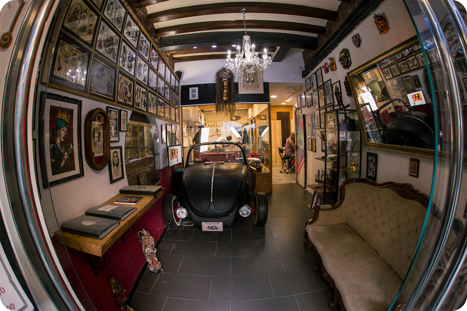 Interno dello studio Trip n' Tattoo nel Quartiere Gotico di Barcellona: un Maggiolino Volkswagen d'epoca nero al centro della sala, lampadario di cristallo e pareti coperte di disegni flash