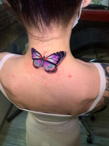 Tatuaje de mariposa realista a color en la nuca.