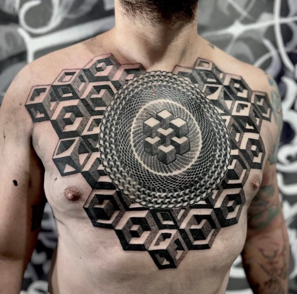Tatuaggio blackwork geometrico sul petto, con cubi tridimensionali e un mandala centrale a puntinato (dotwork), realizzato da Max Sagato presso Trip n' Tattoo, Barcellona