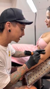 Joni Peralta, artista residente de Trip n' Tattoo, concentrado aplicando tinta negra en un tatuaje detallado en el antebrazo de una chica en el estudio de Barcelona.