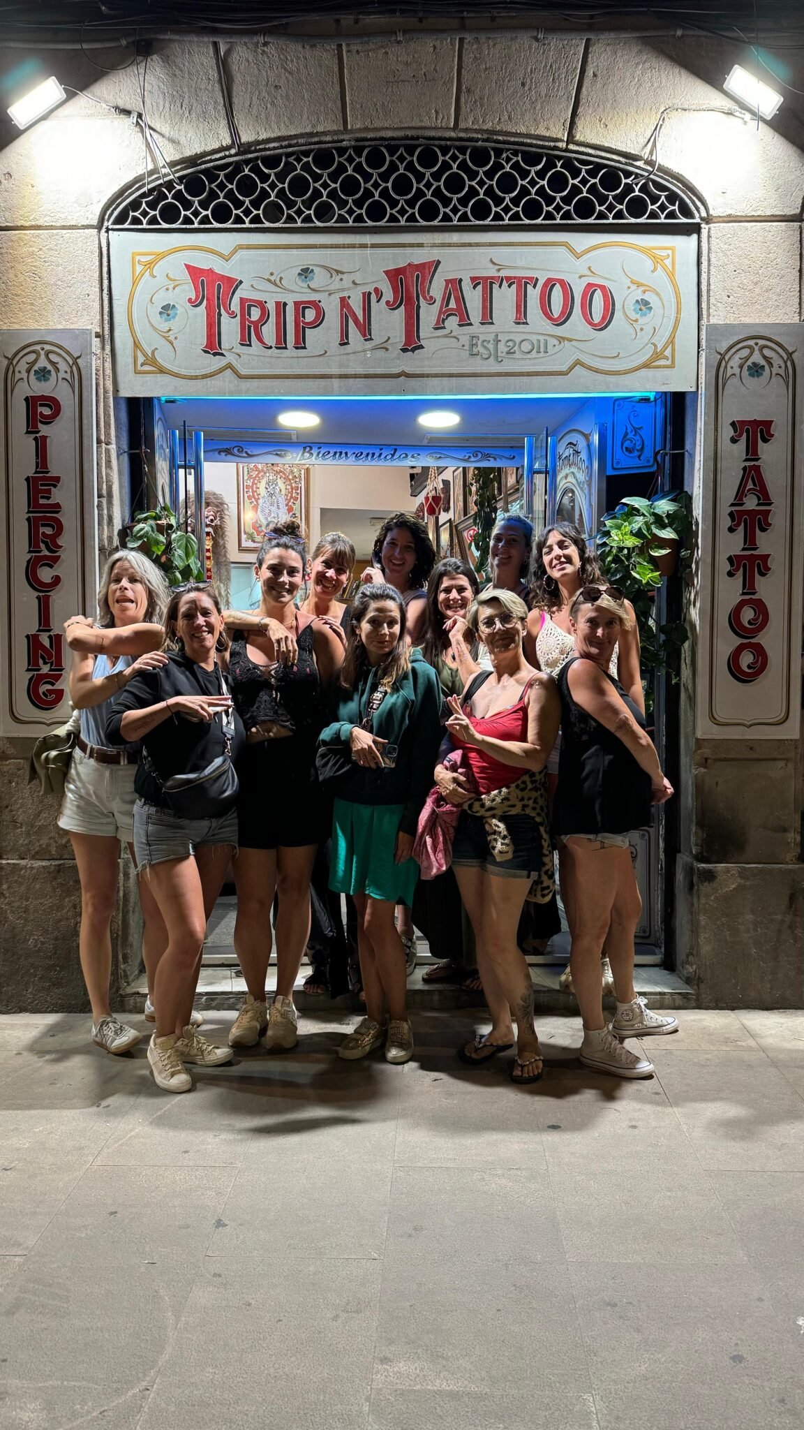 Ingresso dello studio Trip n' Tattoo in Carrer dels Escudellers, nel Quartiere Gotico di Barcellona, con l'insegna dipinta a mano; un gruppo di clienti posa davanti alla porta dopo un tatuaggio walk-in